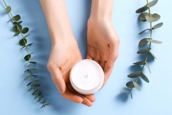 Moisturizing care skincare face cream for healing complicated troubled skin type in an open jar with visible texture. Copy space, close up, background, flat lay, top view. Eucalyptus leaf decoration.
